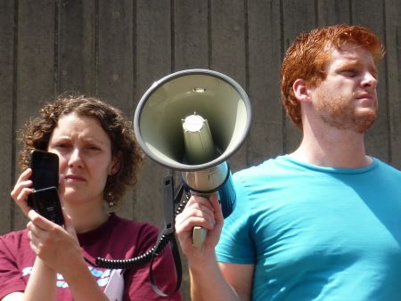 Palmira Boutlier (HMC) and Kyle Buott (Halifax-Dartmouth District Labour Council) hold the megaphone to Miles, reporting via Skype.